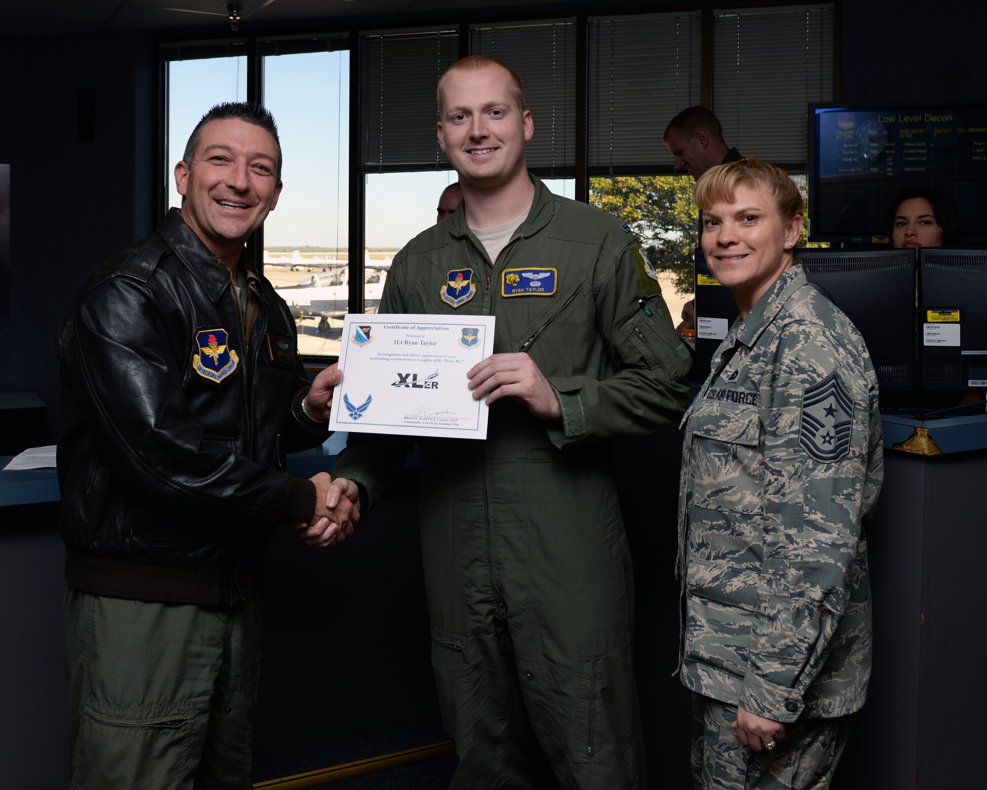 First Lt. Ryan Taylor, center, 85th Flying Training Squadron instructor pilot , poses with Col. Brian Hastings, left, 47th Flying Training Wing commander, and Chief Master Sgt. Teresa Clapper, right, 47th FTW command chief, after being presented the XLer of the week award here Nov. 19, 2014. The XLer is a weekly award chosen by wing leadership and is presented to those who consistently make outstanding contributions to their unit and Laughlin. (U.S. Air Force photo by Airman 1st Class Jimmie D. Pike)(Released)