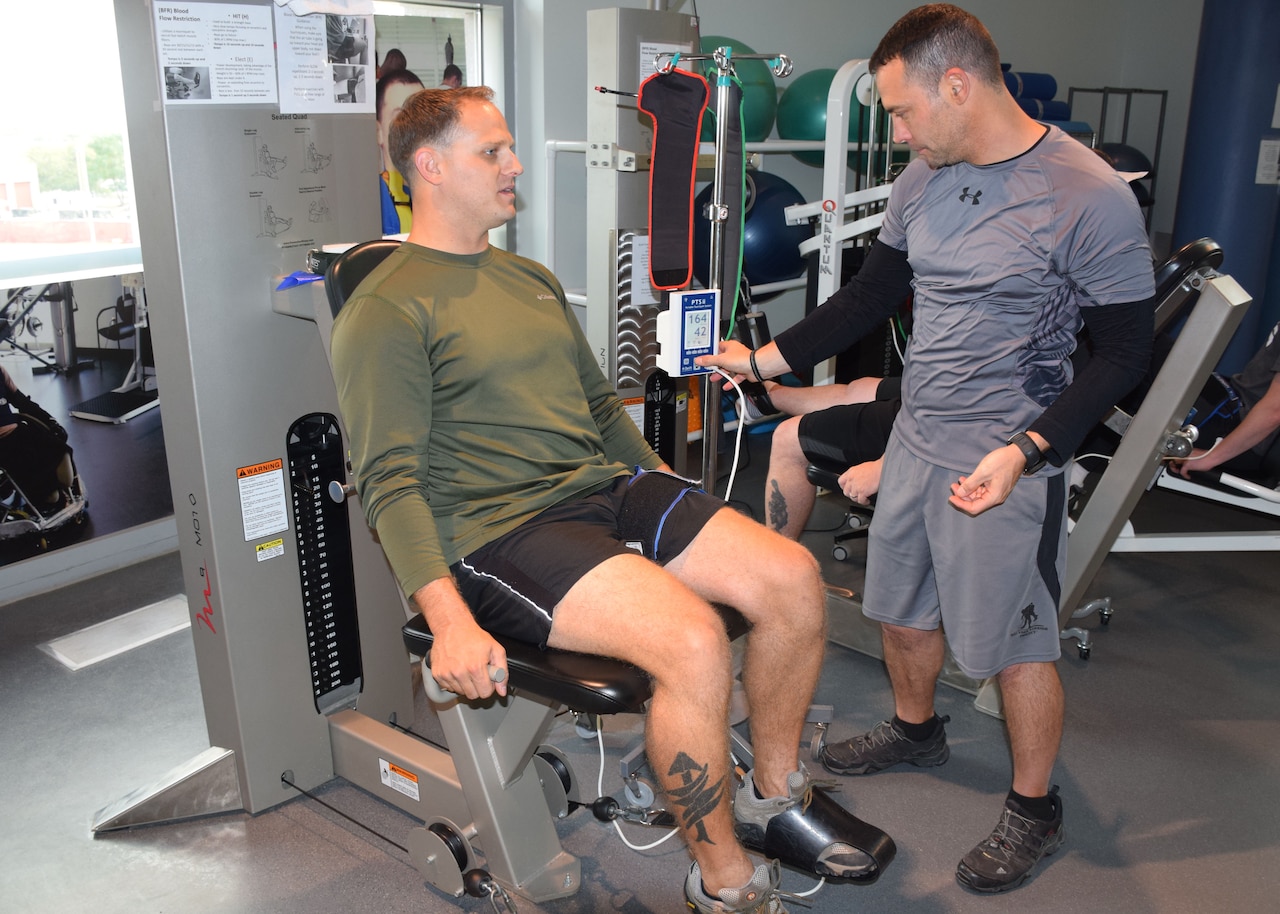 Johnny Owens, chief of the Human Performance Optimization Program, adjusts a setting on a tourniquet worn by Marine Corps Staff Sgt. Brandon Kothman during blood flow restriction training at the Center for the Intrepid’s outpatient rehabilitation center, Brooke Army Medical Center, Texas. Owens implemented the groundbreaking program to help wounded service members build muscle strength and function. U.S. Army photo by Robert D’Angelo