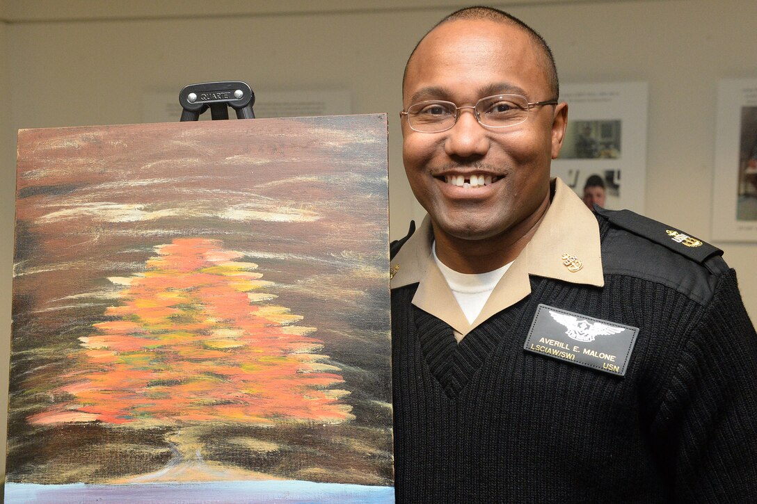 Navy Chief Averill Malone poses for a photo beside one of his paintings during the Warrior Care Month art exhibition at the Pentagon, Nov. 20, 2014. 
