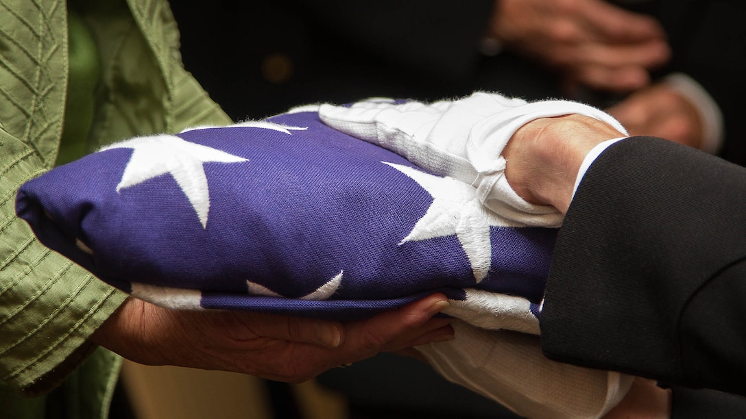 Maj. Stephen Harding, a supply officer with Combat Logistics Battalion 23, presents a flag on behalf of 35th Commandant of the Marine Corps Gen. James Amos to Barbara Kenney during a memorial service for her father, 1st Lt. George Greeley Wells, in Bellevue, Washington, Oct. 25, 2014. Greeley served as the adjutant of 2nd Battalion, 28th Marine Regiment, 5th Marine Division, during World War II’s famed Battle of Iwo Jima. He carried the first flag that was raised on Mt. Suribachi, a moment later captured by Associated Press photographer Joe Rosenthal in the war’s most famous photo. In the 1990s and early 2000s, he was featured in James Bradley’s best-selling book “Flags of Our Fathers” and “War Stories with Oliver North,” produced by the retired Marine and Fox News correspondent. Greeley, a native of Lake Forest, Illinois, moved with his family from Harding Township, New Jersey, to Bellevue in the early 2000s. At 94, he passed away in his sleep here Sept. 22, 2014. 