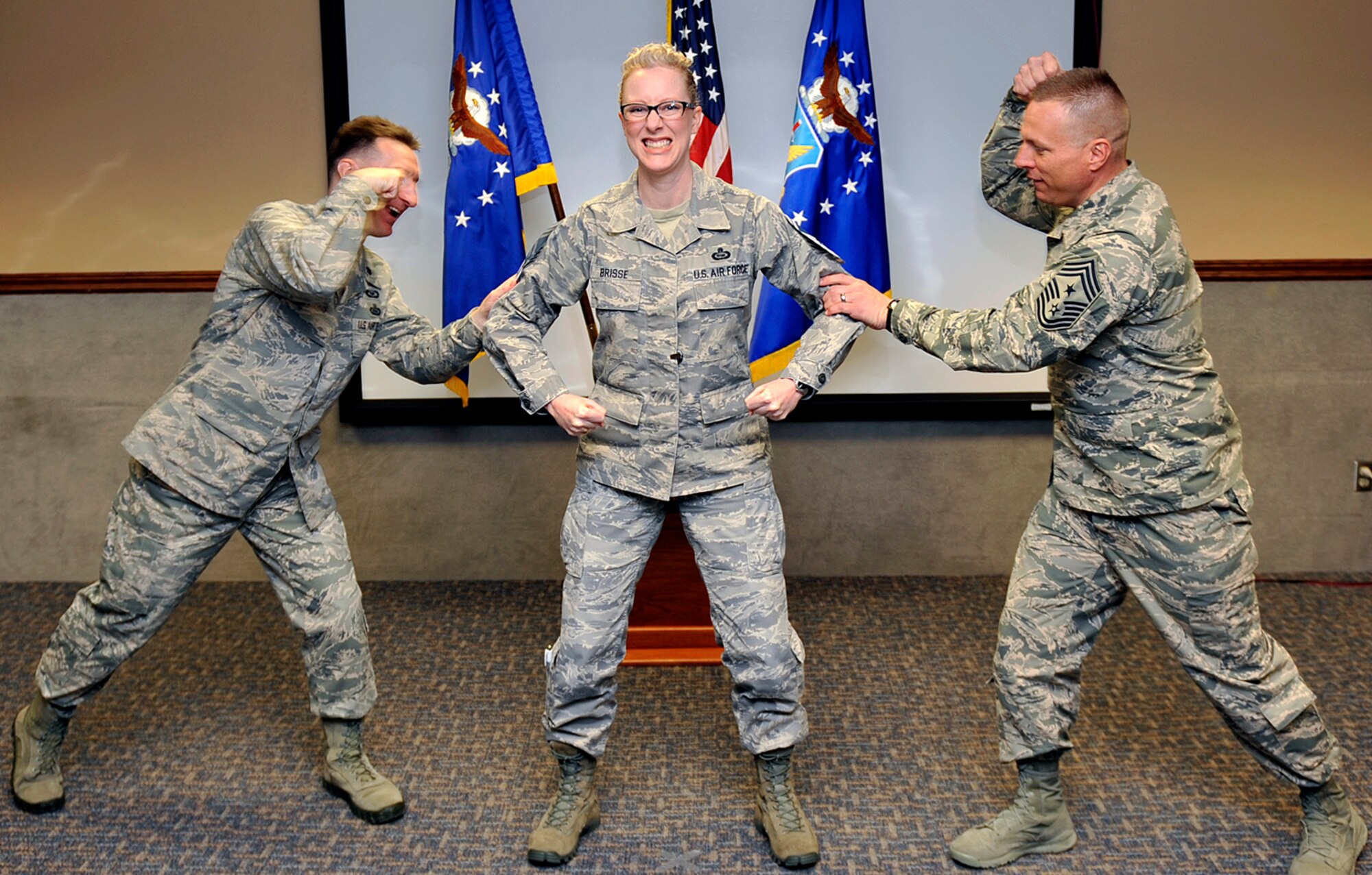 U.S. Air Force Senior Master Sgt. Kellie Brisse, 20th Intelligence Squadron, braces herself as U.S. Air Force Lt. Col. Barrett Morris, 20th IS commander, and U.S. Air Force Chief Master Sgt. Matthew Grengs, 55th Wing command chief, tack on her chief stripes upon being one of nine Team Offutt senior master sergeants selected for promotion to chief as announced by Air Force Personnel Center officials Nov. 20. Air Force-wide, 479 senior master sergeants were selected out of 2,525 eligible for an 18.97 percent selection rate, according to AFPC. (U.S. Air Force photo by Jeff W. Gates/Released)