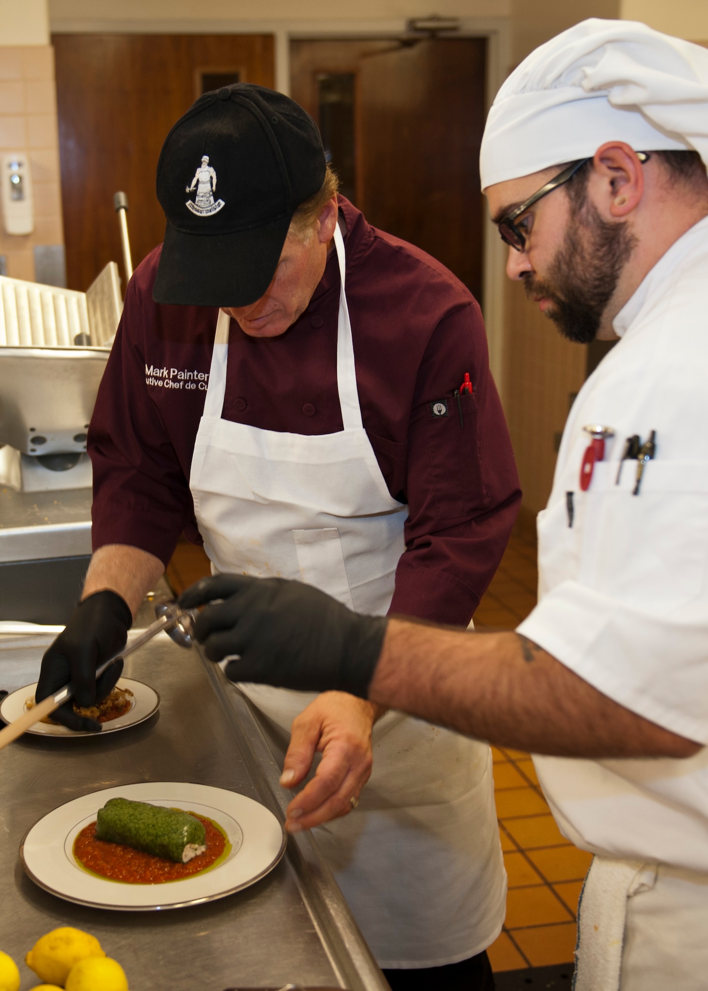 PETERSON AIR FORCE BASE, Colo. – Chef Mark Painter, certified executive chef and instructor at Pikes Peak Community College, left, works with his student and assistant, Tony Baja, to perfect the presentation of the roasted chicken cannelloni for the Celebrity Guest Chef Dinner at the Club Nov. 14. Guests paid $45 to experience a gourmet four course meal prepared by Painter and see a demonstration of how a few of the dishes were created. (U.S. Air Force photo/Airman 1st Class Rose Gudex)