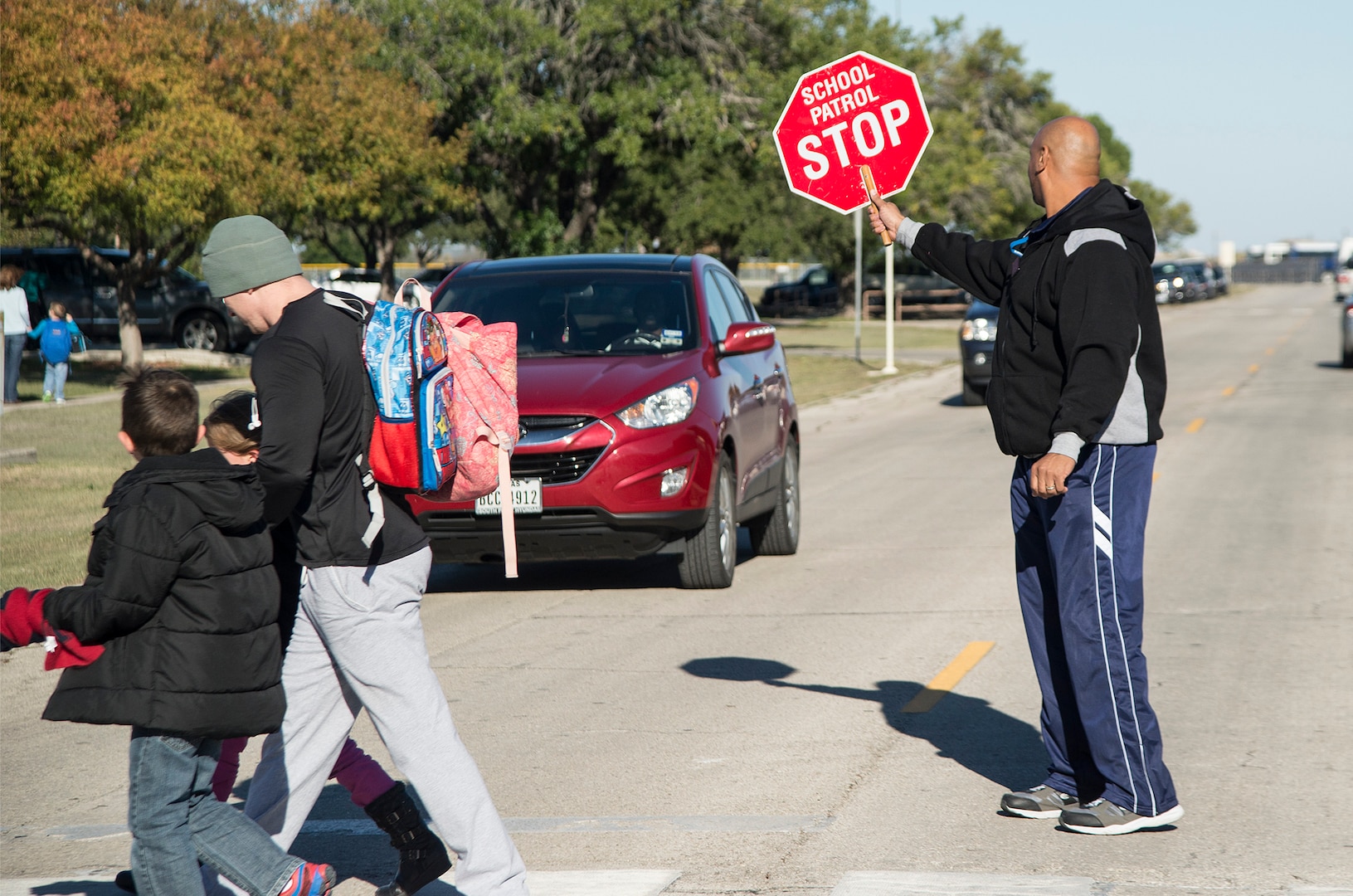 John Collins, Randolph Elementary School teacher’s aide, holds a stop sign to allow parents and their children to safely cross the street Nov. 17 at Joint Base San Antonio, Texas. The 902nd Security Forces Squadron is stepping up its patrols because of speeding problems that pose safety risks to children boarding school buses.  Be alert. Children are unpredictable. Children walking to or from school are usually very comfortable with their surroundings. This makes them more likely to take risks, ignore hazards or fail to look both ways when crossing the street. Drivers are urged to always watch for children crossing traffic lanes, observe school zone speed limits, instructions of crossing guards and use caution when traveling through school zones or near routes used by children. 