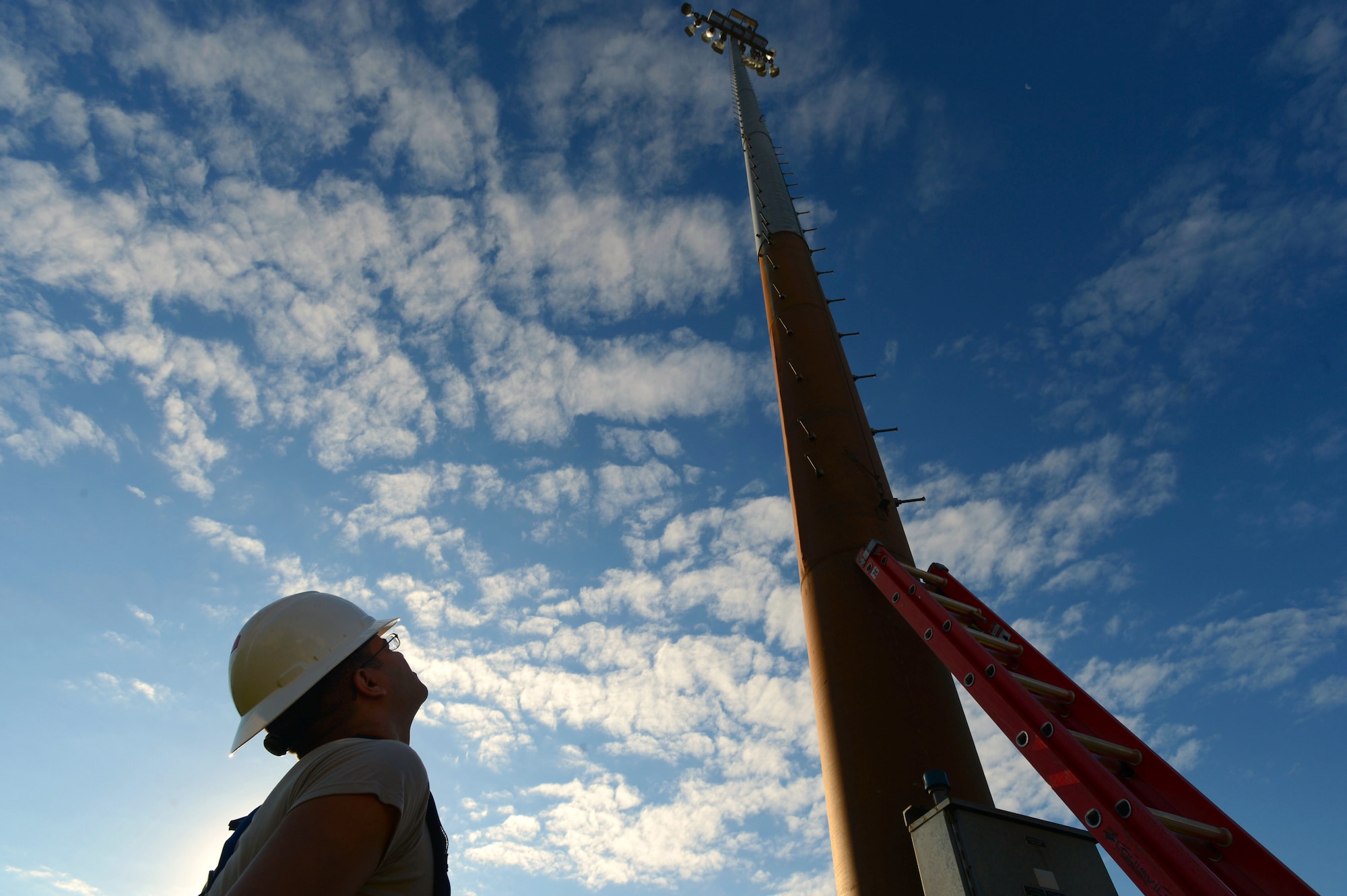 U.S. Air Force Airman 1st Class Daniel Santiago, 20th Civil Engineer Squadron electrical systems journeyman, looks up at a ramp light along the flightline at Shaw Air Force Base, S.C., Oct. 16, 2014. Before being able to perform maintenance on the ramp tower lights, Airmen have to climb the 110 foot pole. (U.S. Air Force photo by Airman 1st Class Jensen Stidham/Released)