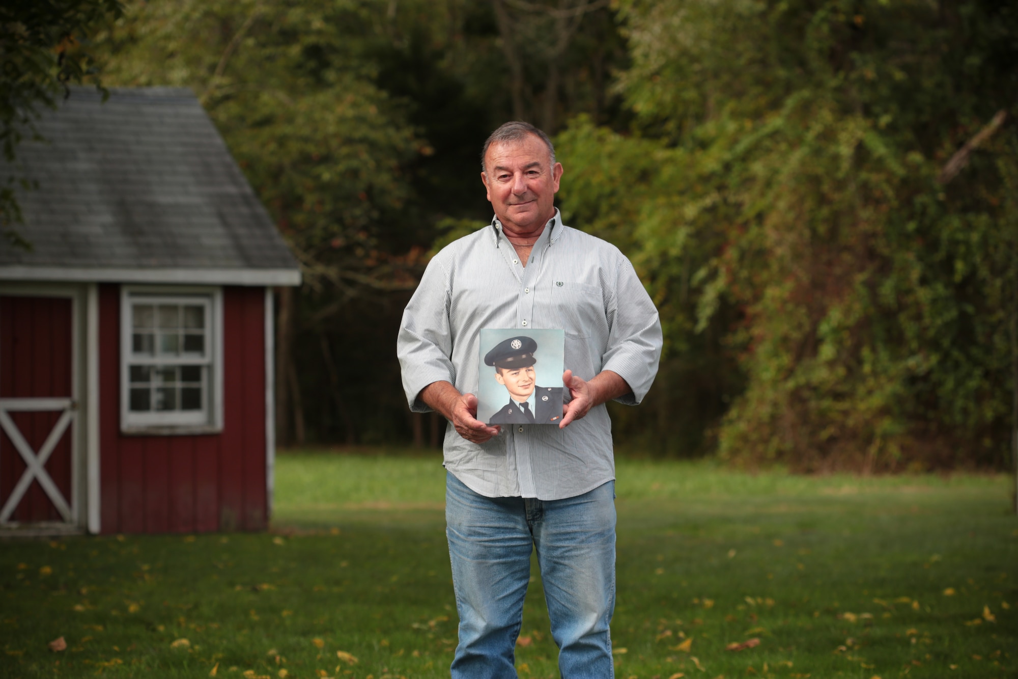 A picture of retired New Jersey Air National Guard Master Sgt. Bob Hensel holding his basic training photo in his backyard.