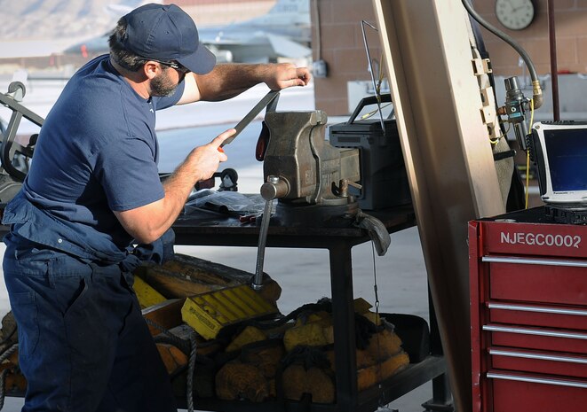 Frank Skanes, a contractor with the 57th Maintenance Group, sharpens a scraper at the Aerospace Ground Equipment hangar on Nellis Air Force Base, Nev., Nov. 20, 2014. The scraper is used to remove items such as, built up material, lettering and numbers from equipment. (U.S. Air Force photo by Airman 1st Class Rachel Loftis) 