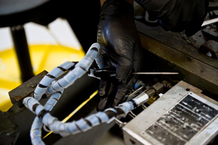 Percy Campbell, a contractor with the 57th Maintenance Group, replaces a hydraulic line on a bomb lift at the Aerospace Ground Equipment hangar on Nellis Air Force Base, Nev., Nov. 20, 2014. AGE workers remove, disassemble, repair, clean, treat for corrosion, assemble and reinstall AGE accessories and components. (U.S. Air Force photo by Airman 1st Class Mikaley Towle) 