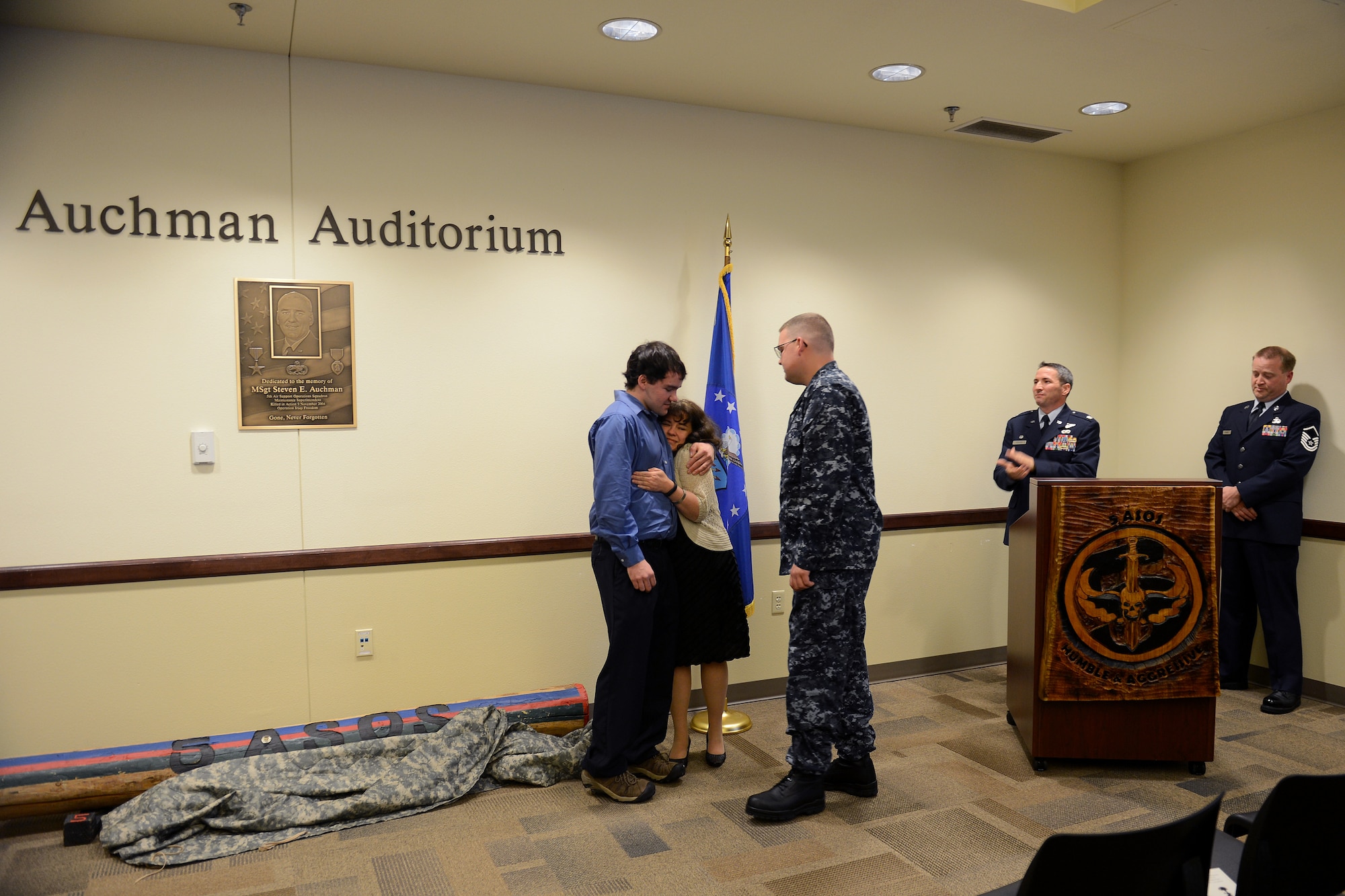 From left to right, Eric, Jennifer, and Brian Auchman, rejoice after uncovering the plaque Nov. 21, 2014, during the Auchman Auditorium Dedication Ceremony at Joint Base Lewis-McChord, Wash. The Auchman Auditorium serves as a small token of remembrance for Master Sgt. Steven Auchman and his family’s sacrifice. (U.S. Air Force photo/Airman 1st Class Keoni Chavarria)