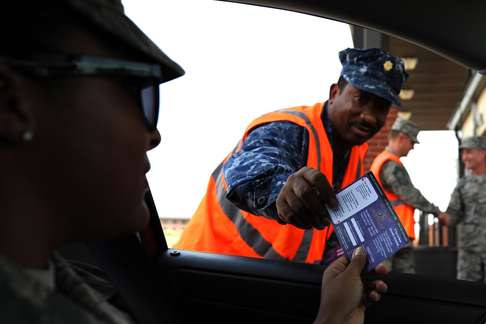 GOODFELLOW AIR FORCE BASE, Texas – Navy Lt. Cmdr. Cornell A. Woods, Center for Information Dominance Detachment Officer in Charge, gives a 17th Training Wing wingman card to a Goodfellow member at the Jacobson Gate July 3. The wingman cards contain important organization numbers such as Airmen Against Drunk Driving, local cab services, 17th Security Forces Squadron, Sexual Assault Response Coordinator hotline and more. (U.S. Air Force photo/ Airman 1st Class Devin Boyer)