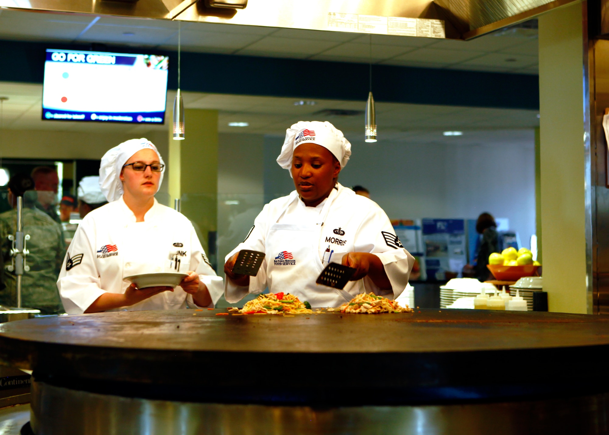 Staff Sgt. Michele Morris and Senior Airman Brittany Junk, 90th Force Support Squadron, cooks a customer's meal on a Mongolian grill Nov. 21, 2014 during the grand opening of the Chadwell Dining Facility on F.E. Warren Air Force Base, Wyo. Warren is the first Air Force base to have a Mongolian Grill in the DFAC. (U.S. Air Force photo/Lan Kim)