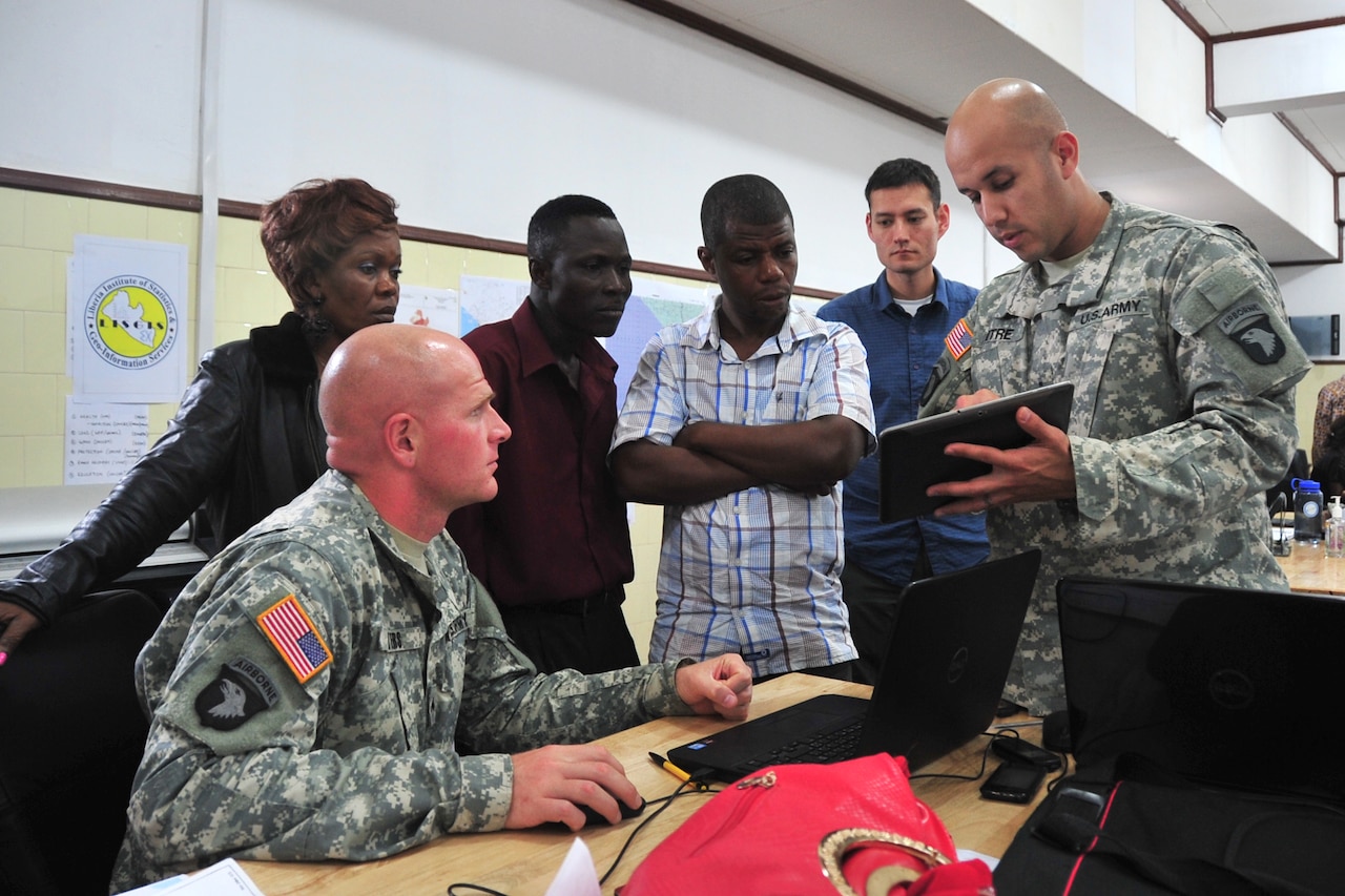 Army Chief Warrant Officer 2 Angel Mitre, right, the Joint Forces Command United Assistance liaison officer to the National Ebola Crisis Center in Monrovia, Liberia, explains to personnel from the Liberian Institute of Statistics Geo-Information Services how an exchange of geospatial data between the JFC-UA and LISGIS created a more robust, useful product for organizations supporting Operation United Assistance, Oct. 29, 2014. Also pictured, from left to right, are Kayloe R. Frank, LISGIS technician; Cpl. Christopher Byers, geospatial information services mentor for JFC-UA; James Z. Barzon, LISGIS technician; Andy Tugbah, LISGIS technician; and Barry Miller, a geospatial intelligence analyst from the National Geospatial-Intelligence Agency. DoD photo