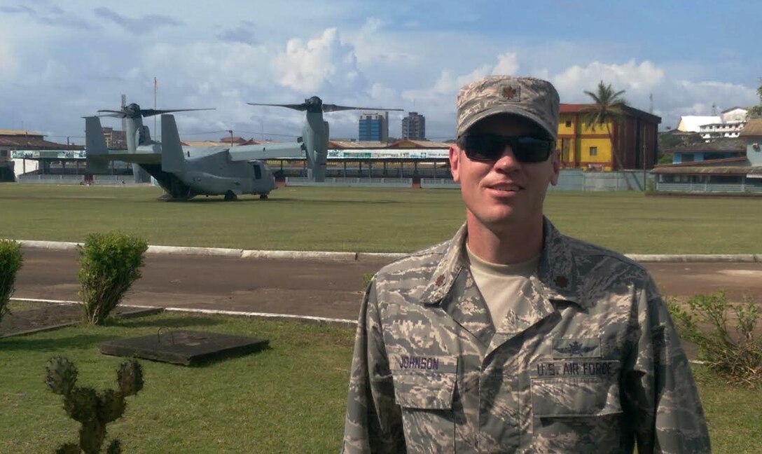 Maj. Kyle Johnson, Africa Command detachment commander, 2nd Joint Communications Squadron, Joint Communications Support Element, pauses for a photo in front of an MV-22 Osprey; the city of Monrovia, Liberia, rises in the background.