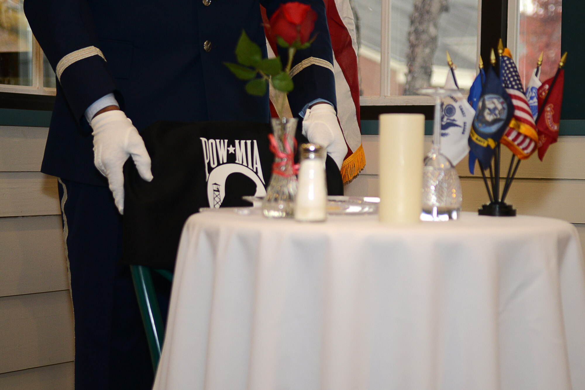 U.S. Air Force Master Sgt. Elroy Williams, 633rd Force Support Squadron community programs manager, sets a POW/MIA chair cover on a chair near a POW/MIA dedication table in the Crossbow Dining Facility at Langley Air Force Base, Va., Nov. 25, 2014. The POW/MIA symbol depicts the silhouette of a man on a white disk with a watch tower, a guard on patrol and a strand of barbed wire in the background. Below the disk is a wreath, above the motto, “You Are Not Forgotten.” The late Newt Heisley, an Army Air Core pilot during WWII, designed the image in 1971. (U.S. Air Force photo by Airman 1st Class Devin Scott Michaels/Released)