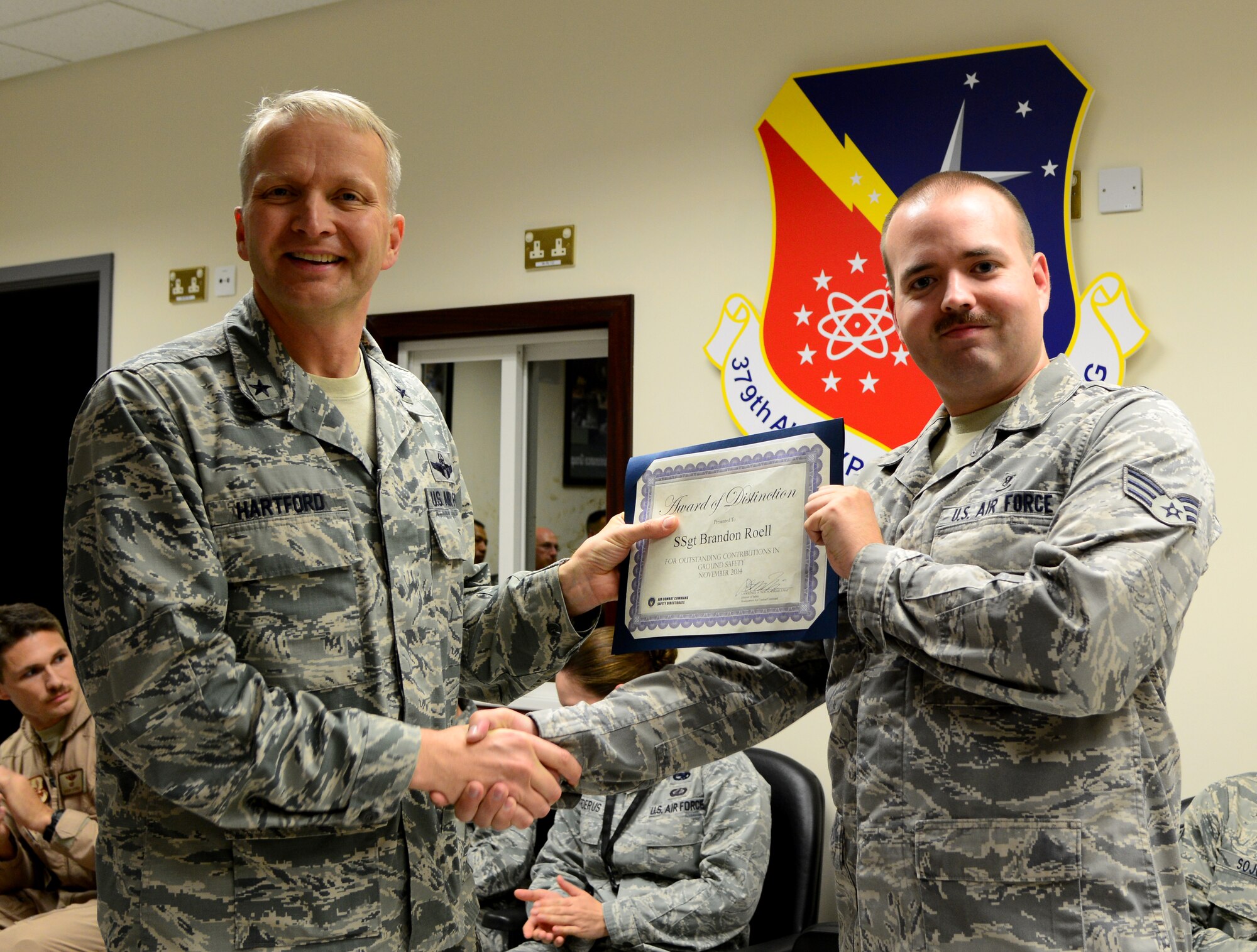 U.S. Air Force Brig. Gen. Darren Hartford, 379th Air Expeditionary Wing commander, presents Senior Airman Brandon Roell, 379th Expeditionary Medical Support Squadron radiology technologist, with an Award of Distinction for his outstanding contribution to ground safety, Nov. 28, 2014, at Al Udeid Air Base, Qatar. While reading the American Journal of Roentgenology, Roell  discovered that new computed tomography (CT) parameters have the potential to reduce a patient's radiation dose while maintaining the quality of the diagnostic images. He used this knowledge, combined with his previous experience, to engineer new CT scanning protocols, which ultimately results in improved safety for patients. (U.S. Air Force photo by Senior Airman Kia Atkins)