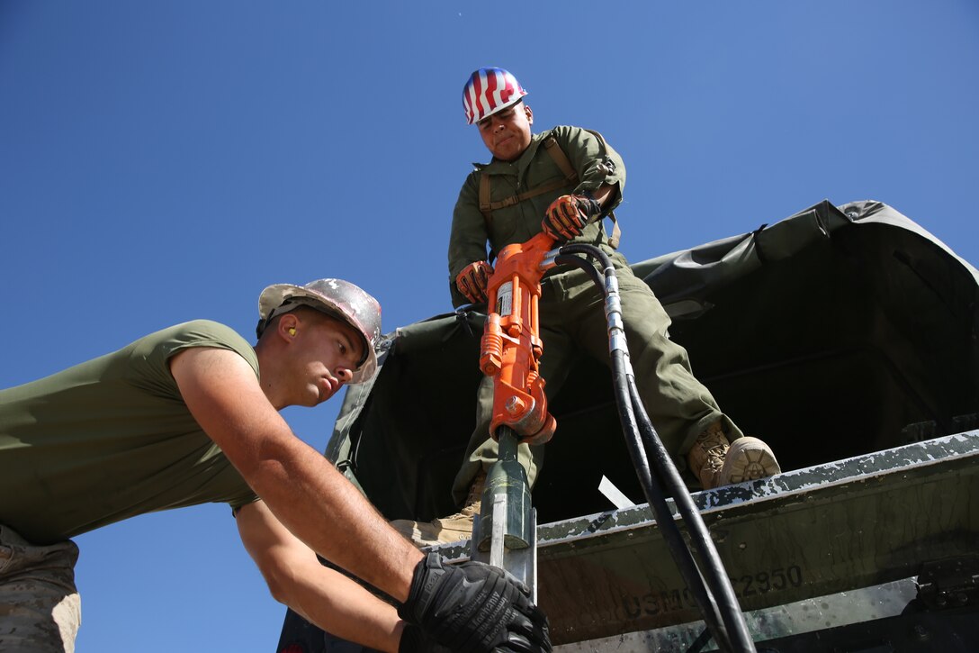 Lance Cpl. Romen Hines, crew member, Marine Wing Support Squadron 374, and Lance Cpl. Timothy Sakaida, crew member, MWSS 374, jackhammer stakes to anchor panels into the ground at the Strategic Expeditionary Landing Field, Camp Wilson, Sept. 29, 2014.