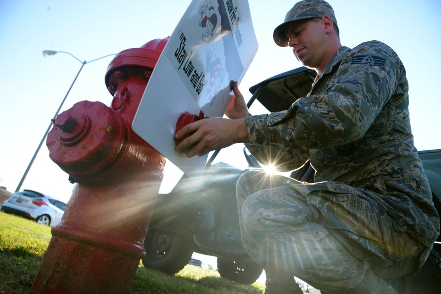 U.S. Air Force Senior Airman Jeremy Brannock, 20th Civil Engineer Squadron firefighter, attaches a sign to a fire hydrant at Shaw Air Force Base, S.C., Oct. 01, 2014. The signs are part of a marketing campaign by the 20th CES fire department to raise awareness for National Fire Prevention Week, Oct. 6-11. During the week, fire department personnel are scheduled to go around base to speak to service members and families about fire prevention techniques, exit procedures, and fire safety. (U.S. Air Force photo by Airman 1st Class Jonathan Bass/Released)