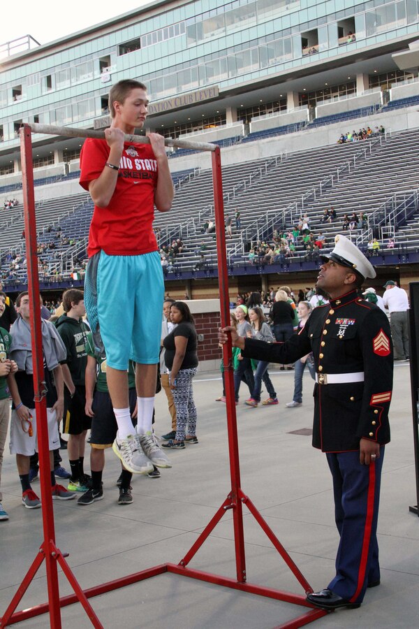 U.S. Marine Corps Sgt.  Ryan Johnson, recruiter at Recruiting Sub-Station Akron and Gary, Indiana, native, steadily holds the pull-up bar for a participant of the pull-up challenge during the Great American Rivalry Series Game featuring St. Vincent St. Mary versus Archbishop Hoban at University of Akron’s InfoCision Stadium, Sept. 26, 2014.  The pull-up challenge gave fans the chance to earn points in an effort to win the Pull-up Challenge Spirit Award for their respective school. Archbishop Hoban won the challenge, surpassing St. Vincent St. Mary fans by over 100 pull-ups (U.S. Marine Corps photo by Sgt. T.M. Stewman/Released)