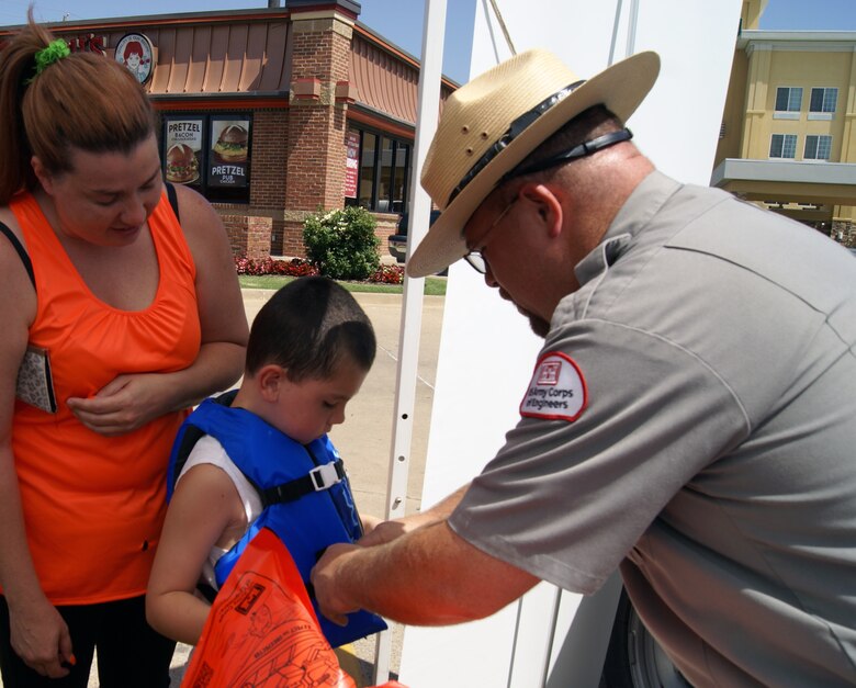 Tulsa District Park Ranger Jason Person fits a child with a life jacket at the Water Safety Day held July 13. Safe Kids provided more than 100 free life jackets to children that day.                  