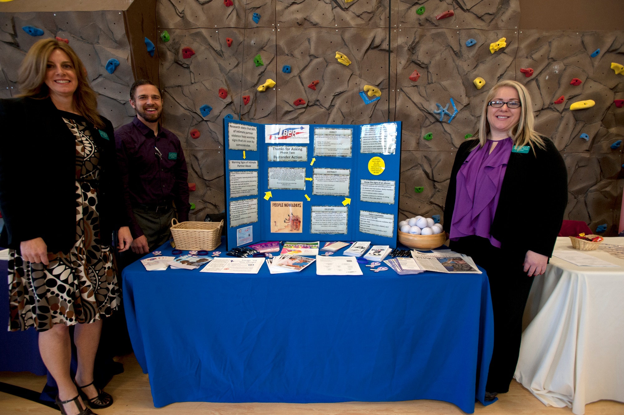 Diann Richardson, far left, Daniel Francom and Jennifer Frysz man a ‘Thanks for Asking Phase 2: Bystander Action” campaign display during a Domestic Violence Prevention Month opening ceremony Oct. 1, 2014 at the Covenant House in Anchorage, Alaska. Richardson, Francom and Frysz are Family Advocacy Outreach managers on Joint Base Elmendorf-Richardson, Alaska. The purpose of the program is to raise awareness about domestic violence and to gauge how many people will question injured volunteers. Nearly one in four women, one in nine men and more than three million children have been affected by domestic violence in the country. According to Department of Defense records, in federal year 2011, 14,237 people in abusive relationships were supported by Family Advocacy. (U.S. Air Force photo/Staff Sgt. Robert Barnett)