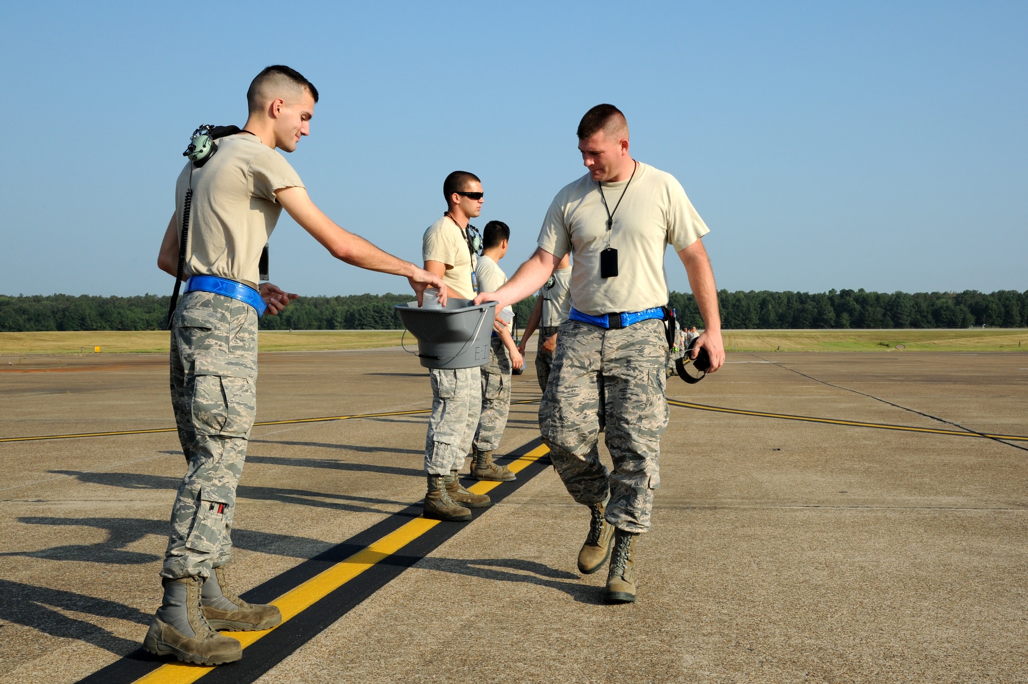 An Airman drops debris he gathered into a bucket during a foreign object debris walk Sept. 9, 2014, at Little Rock Air Force Base, Ark.  A line of Airmen will briefly stop walking to deposit the debris they collected on the flightline. (U.S. Air Force photo by Airman 1st Class Mercedes Muro) 