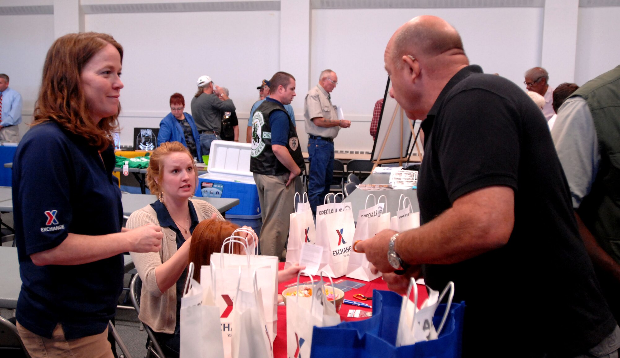 From left, Shawna Turner, shoppette manager, and Chandelle Myers, Army & Air Force Exchange Service sales representative, hand out gift bags to military retirees Sept. 27, 2014, at the Community Activity Center on Grand Forks Air Force Base, N.D. AAFES was one of several base organization to participate in the yearly event. (U.S. Air Force photo/Staff Sgt. Susan L. Davis)