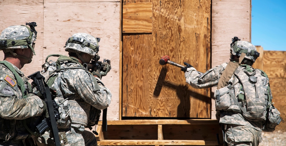 A soldier uses a sledge hammer to break down a door to gain entry to a building after breaching an enemy compound during rotation 14-10 at the National Training Center on Fort Irwin, Calif., Sept. 18, 2014.