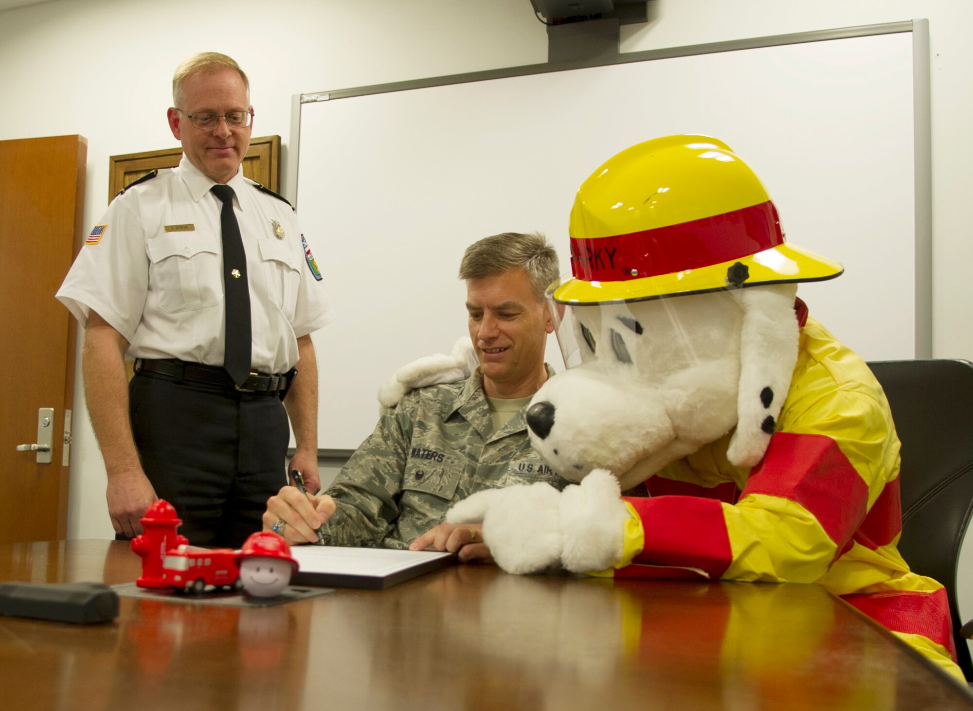 Chief Timothy Pitman, 11th Wing Civil Engineer Squadron Fire Department chief, and Col. Daniel Waters, 11th Wing vice commander, sign the Fire Prevention Week proclamation with Sparky, the fire house dog, on Joint Base Andrews, Md., Oct. 3, 2014. This year, in hopes to better educate the public about the true value of working smoke detectors, the slogan for Fire Prevention Week is ‘Working smoke alarms save lives, test yours every month!’ (U.S. Air Force photo by Senior Airman Mariah Haddenham/Released)