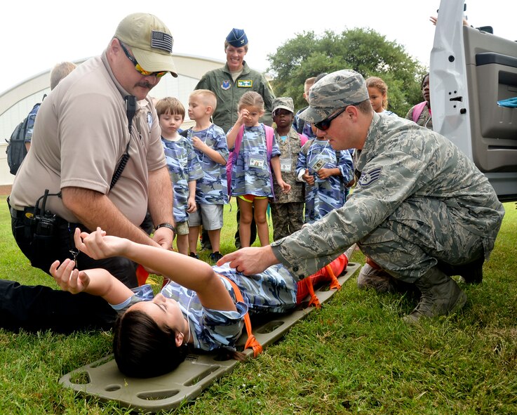 Staff Sgt. Matt McCloud, 2nd Medical Operations Squadron medic, and Robert Cline, 2nd MDOS paramedic, demonstrate the use of a stretcher on Barksdale Air Force Base, La., Sept. 27, 2014. Operation Hero aims to demonstrate to children the tools available to keep their parents safe during deployments. (U.S. Air Force photo/Airman 1st Class Mozer O. Da Cunha)