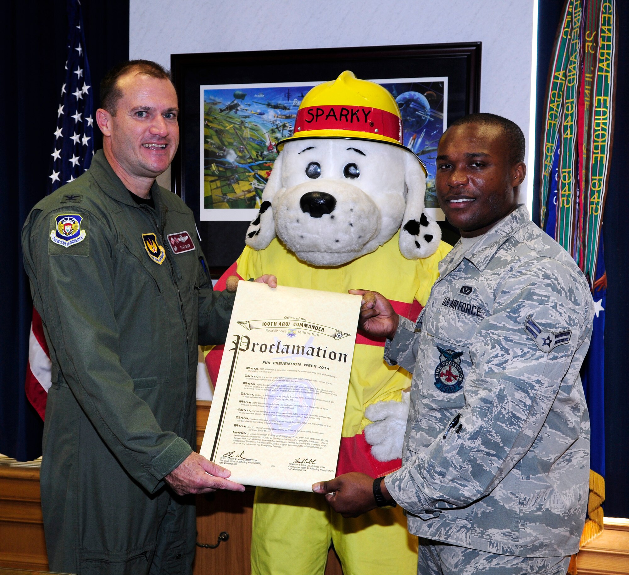 U.S. Air Force Col. Kenneth T. Bibb Jr., left, 100th Air Refueling Wing commander; Sparky the Fire Dog and U.S. Air Force Airman 1st Class Kaylon Centers, 100th Civil Engineer Squadron Fire Department fire protection apprentice from Longview, Texas, show off the signed proclamation marking the upcoming Fire Prevention Week Oct. 3, 2014, at the 100th ARW headquarters building on RAF Mildenhall, England. Fire Prevention Week is held annually and provides continued education for service members and their families on responding to fires. (U.S. Air Force photo/Karen Abeyasekere/Released) 