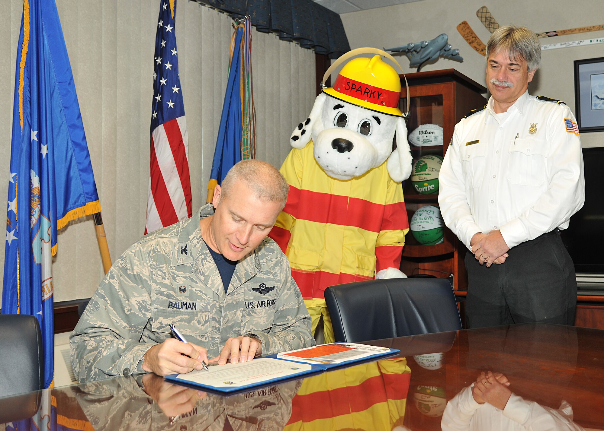 Col. Paul Bauman, 319th Air Base Wing commander, signs the 2014 Fire Prevention Week proclamation as Assistant Fire Chief Merele McCreary, and Sparky the Fire Dog look on Oct. 3, 2014 at the wing headquarters building on Grand Forks Air Force Base, N.D. The signing of the proclamation officially kicked off the base's fire prevention week events, which will run from Oct. 5-11 and is coordinated by the Grand Forks Air Force Base Fire Department. (U.S. Air Force photo/Senior Airman Xavier Navarro)