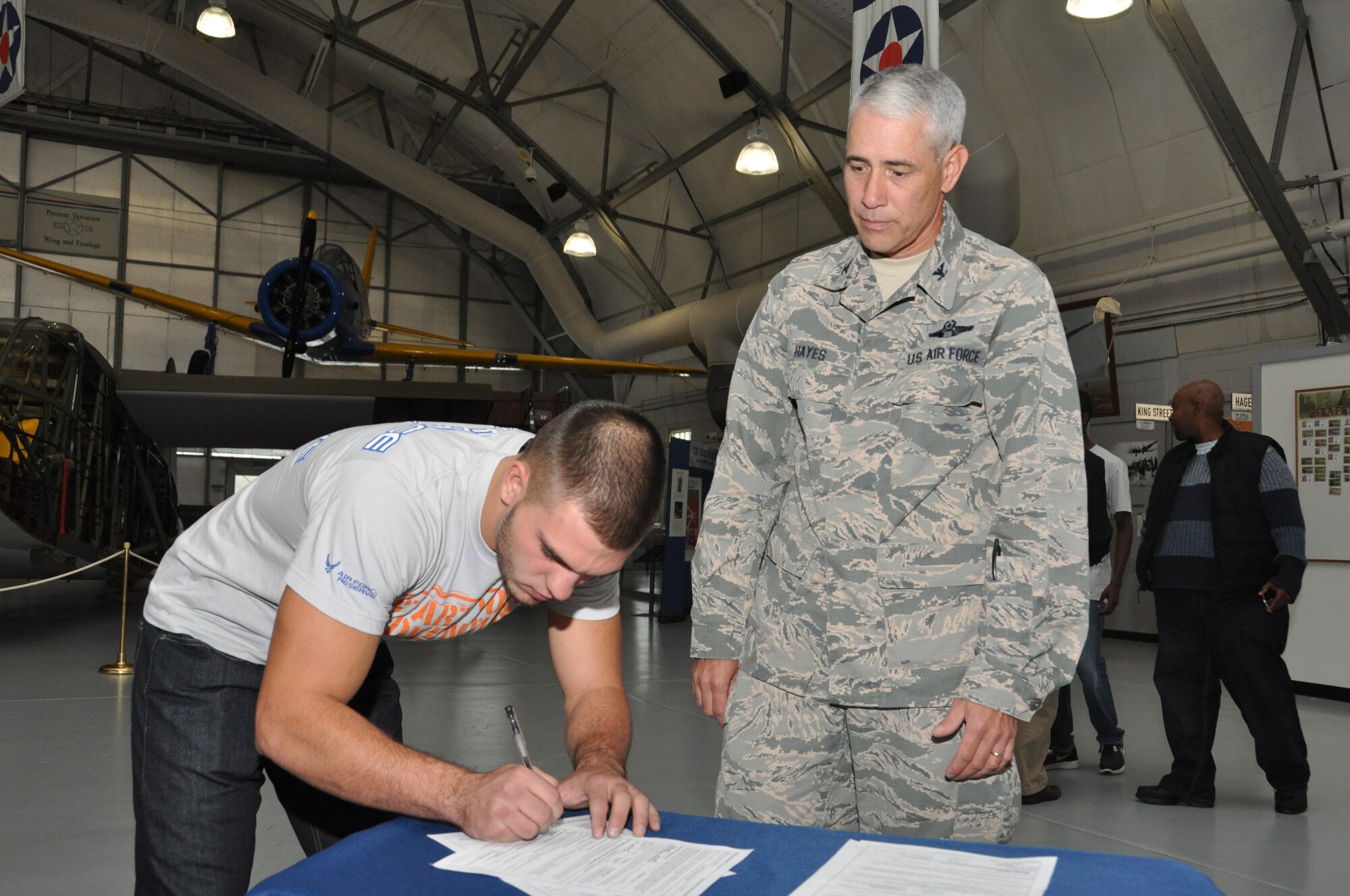 Col. J. Scott Hayes, 512th Airlift Wing vice commander, observes Nathaniel Turnbull as he signs an enlistment contract for the Air Force Reserve Oct. 4, 2014, at the Air Mobility Command Museum, Dover, Del. Hayes administered the oath of enlistment to Turnbull and five others during a mass enlistment ceremony before a crowd of family and friends from Delaware, Maryland and Pennsylvania. (U.S. Air Force photo/Senior Airman Joe Yanik)