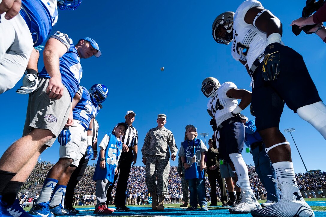 Members of the U.S. Air Force Academy and U.S. Naval Academy football teams watch as Army Gen. Martin E. Dempsey, chairman of the Joint Chiefs of Staff, flips the game coin into the air before the start of the Air Force vs. Navy game at Falcon Stadium in Colorado Springs, Colo., Oct. 4, 2014. Air Force won the game, 30-21. 