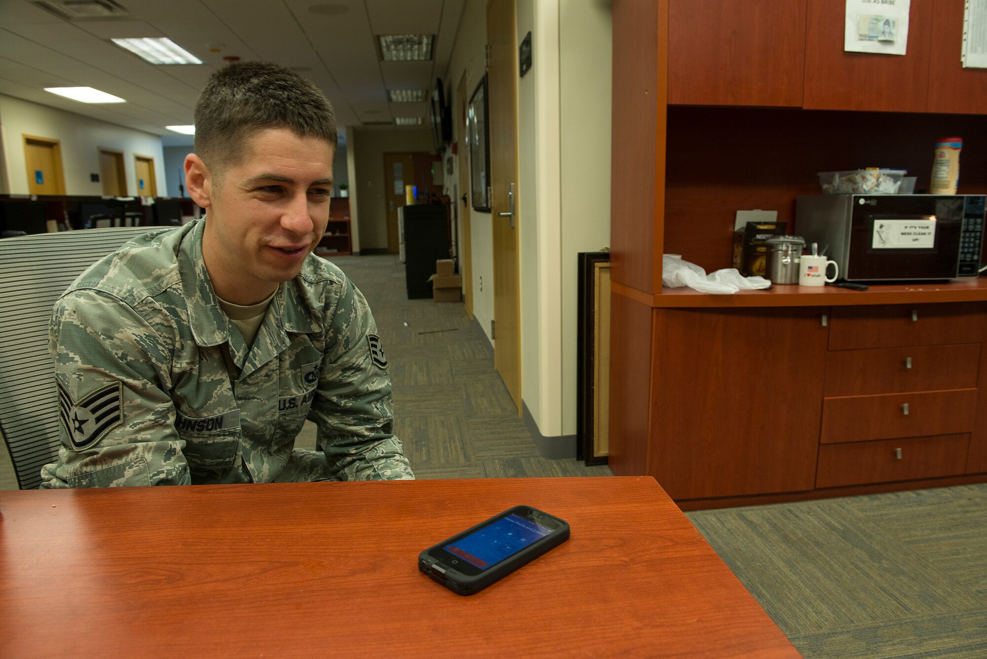 Staff Sgt. Joshua Johnson, a 51st Operations Support Squadron airfield management operations supervisor, listens to his mother sing "Happy Birthday" for him on the phone at work Aug. 23, 2014, at Osan Air Base, Republic of Korea. Family is important to Johnson, who credits his mother with teaching him to be humble and serve others. (U.S. Air Force photo by Staff Sgt. Jake Barreiro/Released)