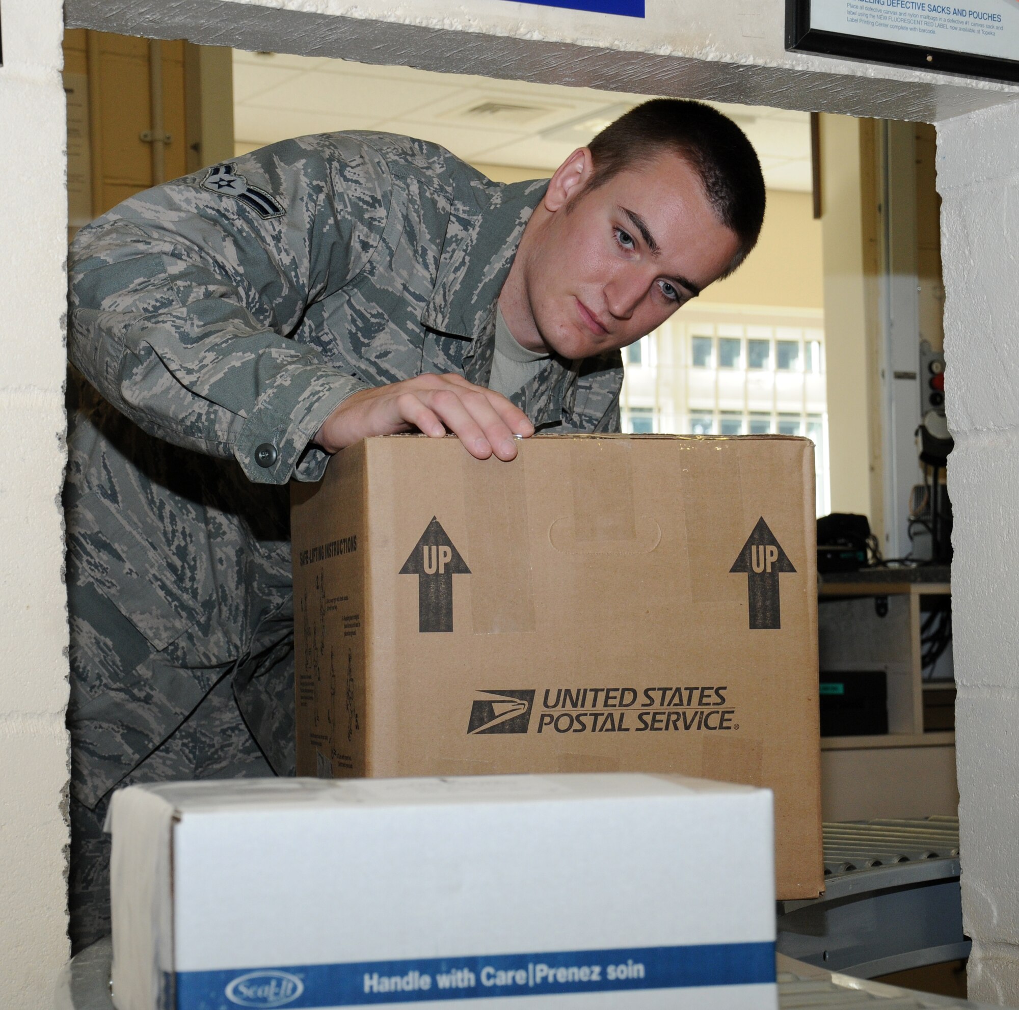 U.S. Air Force Airman 1st Class Kyle Hunt, 100th Communications Squadron postal clerk from Mission Viejo, Calif., collects a box for a customer Oct. 1, 2014, on RAF Mildenhall, England. The post office is open to serve Department of Defense employees and their dependents. (U.S. Air Force photo/Gina Randall/Released)