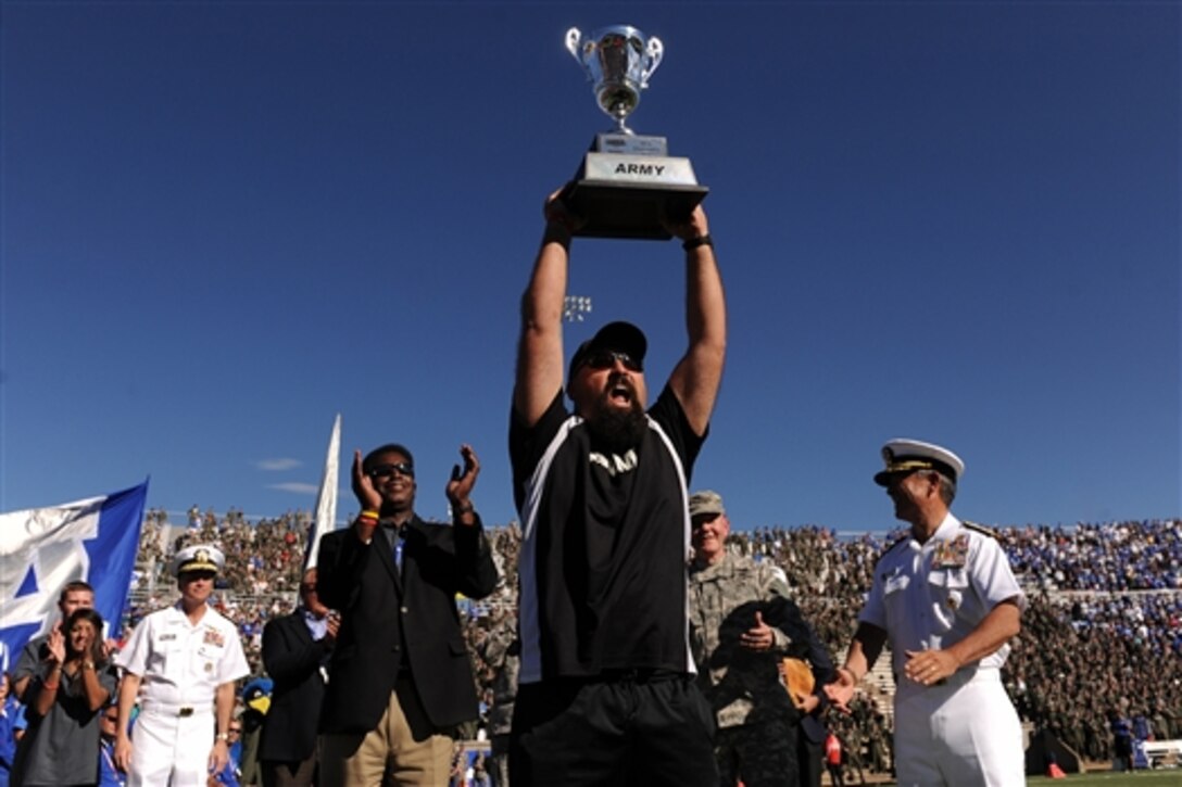 Team Army captain Frank Barroqueiro raises the Chairman's Cup presented to him by Army Gen. Martin E. Dempsey, chairman of the Joint Chiefs of Staff, center right, and Navy Adm. Harry B. Harris, commander of the Pacific Fleet, right, at the U.S. Air Force Academy's Falcon Stadium in Colorado Springs, Colo., Oct. 4, 2014. The Chairman's Cup goes to the top performing service branch in the Warrior Games, an adaptive sports competition for wounded, ill and injured service members and veterans. 