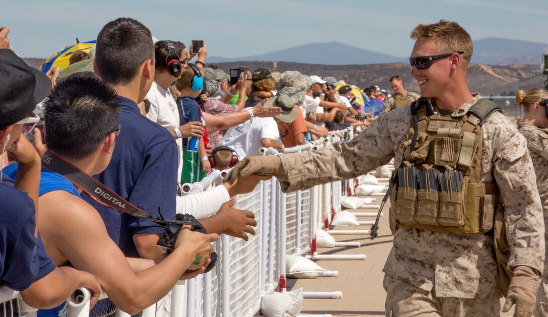 Spectators extend their hands and cheer as infantry Marines perform a final pass and review after the Marine Air-Ground Task Force demonstration during the Miramar Air Show aboard Marine Corps Air Station Miramar, Calif., Oct. 3. These Marines made their appearance as the ground portion of the force, suppressing the enemy on land while aircraft provided cover fire from above.