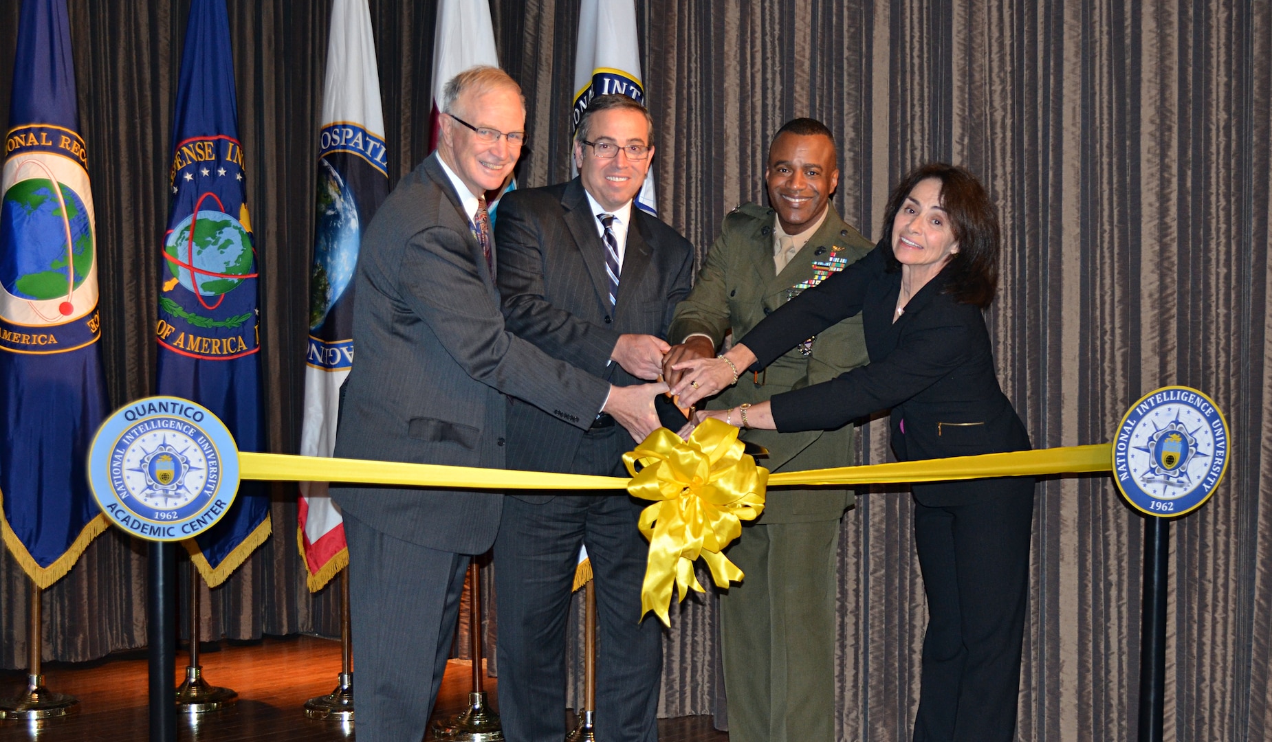 “Today is a great day for Quantico, a great day for National Intelligence University (NIU) and a great day for the intelligence and national security communities!” said Maureen Baginski (shown, far right) as she helped cut the ribbon to mark the formal opening of NIU’s Quantico Academic Center in partnership with the FBI and Marine Corps Intelligence Activity.  “These three organizations worked together to achieve something none could have achieved on their own while taking care of the most important Intelligence Community asset: our people!”   Shown from left to right, Dr. David Ellison, NIU President; Eric Velez-Villar, FBI Executive Assistant Director for Intelligence; Col Melvin Carter, Commanding Officer, Marine Corps Intelligence Activity, and Maureen Baginski, Chair of the NIU Board of Visitors.