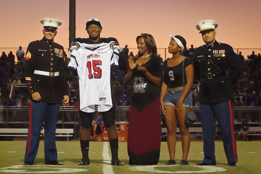 Caleb Peart, a defensive end for Hamilton High School in Chandler, Ariz. and a 2015 Semper Fidelis All-American, receives a jersey during a presentation by Arizona Marines on his home field before Hamilton's rival matchup versus Chandler H.S., Oct. 2, 2014. The Semper Fidelis Football Program brings together the nation’s best and brightest high school football players from across the country, who demonstrate success both on and off the gridiron. Peart, a team captain, attributes his determination and resilience to his mother, Jackie, joining him in the presentation with his sister. "A lot of things parallel with football and life. As far as being resilient and hard working, I think you can take those from the football field into the real world when you have a real job and a family 15-20 years down the road," said Peart. (U.S. Marine Corps photo by Sgt. Tyler J. Bolken)