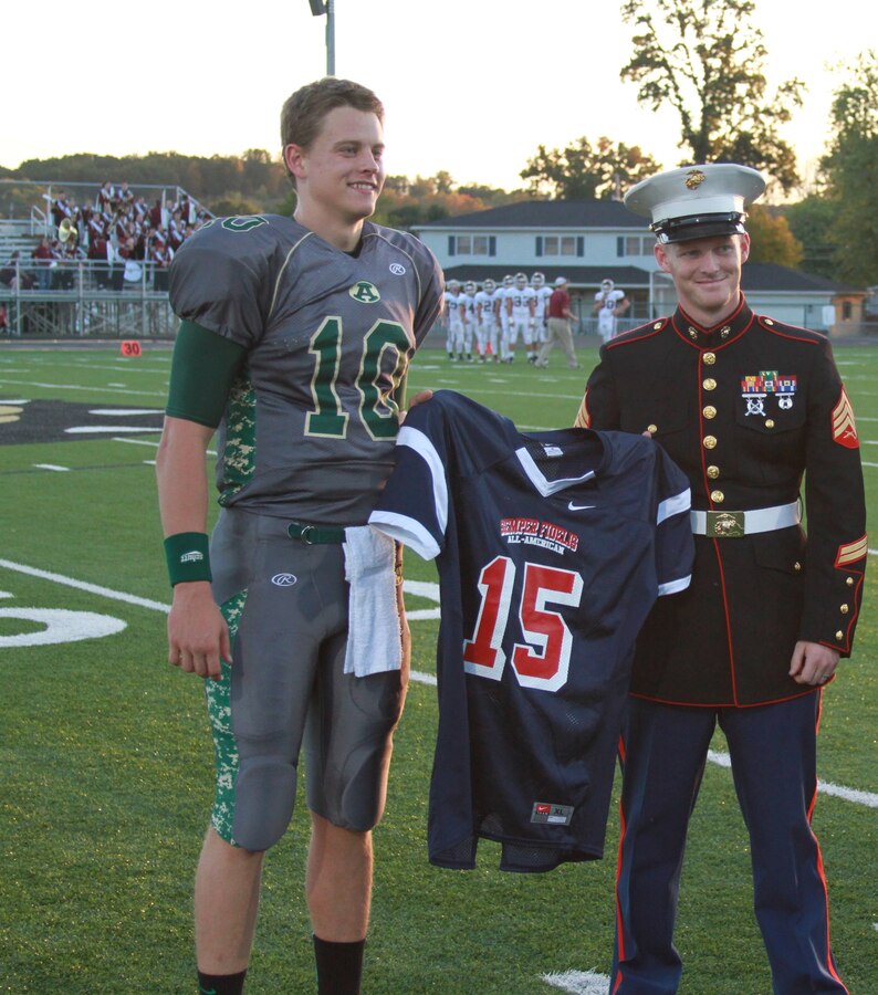 U.S. Marine Corps Sgt. David A. Wood, a recruiter for the Athens, Ohio, area, presents a jersey to Athens High School quarterback Joe Burrow during a presentation conducted at the Athens Football Stadium Sept. 27, 2014. Burrow has been officially selected to play in the Marine Corps Semper Fidelis All American Bowl, which will be held Jan. 4, 2015 in Carson, California. 