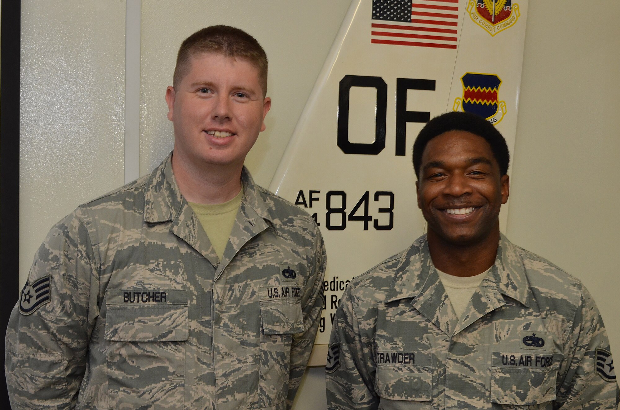 U.S. Air Force Staff Sgt. Hassell Butcher, 82nd Reconnaissance Squadron aerospace hydraulics systems craftsman, and Staff Sgt. Darnell Strawder, 82nd RS aerospace propulsion craftsman, are pictured standing in front of their squadron's logo on Kadena Air Base, Japan, Oct. 8, 2014. These Airmen used their self-aid and buddy care skills to assist a scooter driver who struck the side of a van erupting the fuel tank of his scooter. (Courtesy photo)