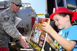 U.S. Air Force Staff Sgt. Nathan Cinq-Mars, 633rd Civil Engineer Squadron firefighter, hands fire safety and prevention goody-bags to children at Bethel Manor Elementary School in Hampton, Va., Oct. 6, 2014. The firefighters visited the school as part of fire prevention week, which is recognized annually. (U.S. Air Force photo by Staff Sgt. Natasha Stannard/Released)