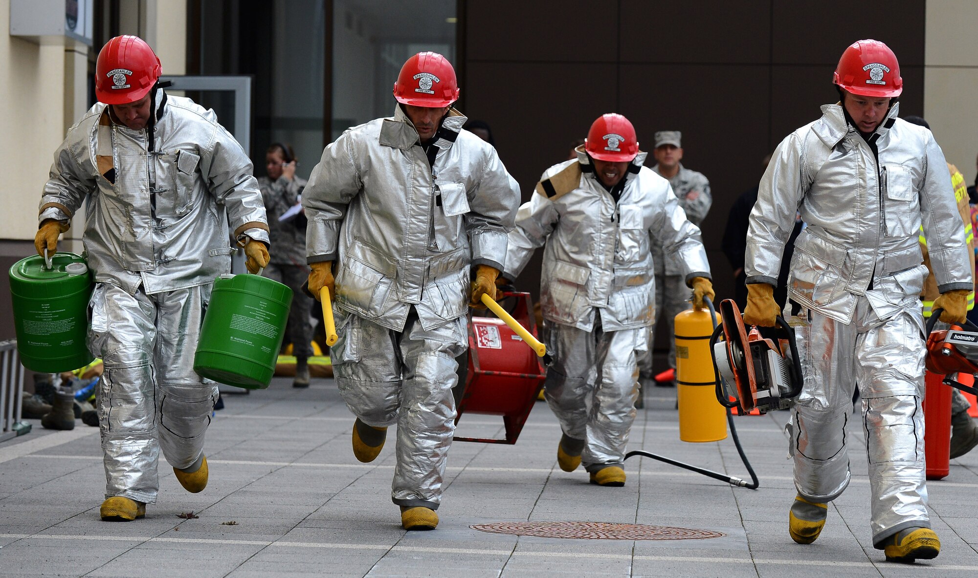 members from the 52nd Force Support Squadron carry firefighting equipment during a Fire Muster Challenge at the Exchange parking lot at Spangdahlem Air Base, Germany, Oct. 6, 2014. The Fire Muster Challenge was one of many events scheduled this week to spread fire prevention awareness. The theme this year is, “A working fire alarm saves lives.” (U.S. Air Force photo by Airman 1st Class Luke J. Kitterman/Released)
