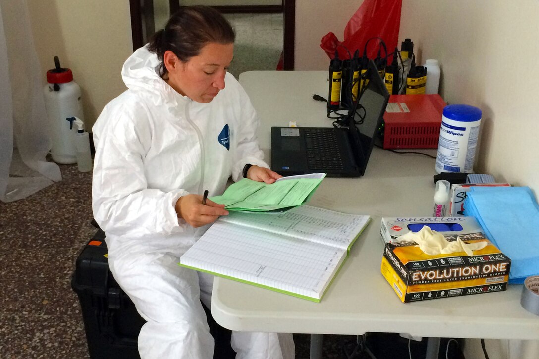 U.S. Navy Lt. Andrea McCoy reviews specimen documentation and records data in a laboratory log book at a Naval Medical Research Center mobile laboratory on Bushrod Island, Liberia, Oct. 6, 2014.