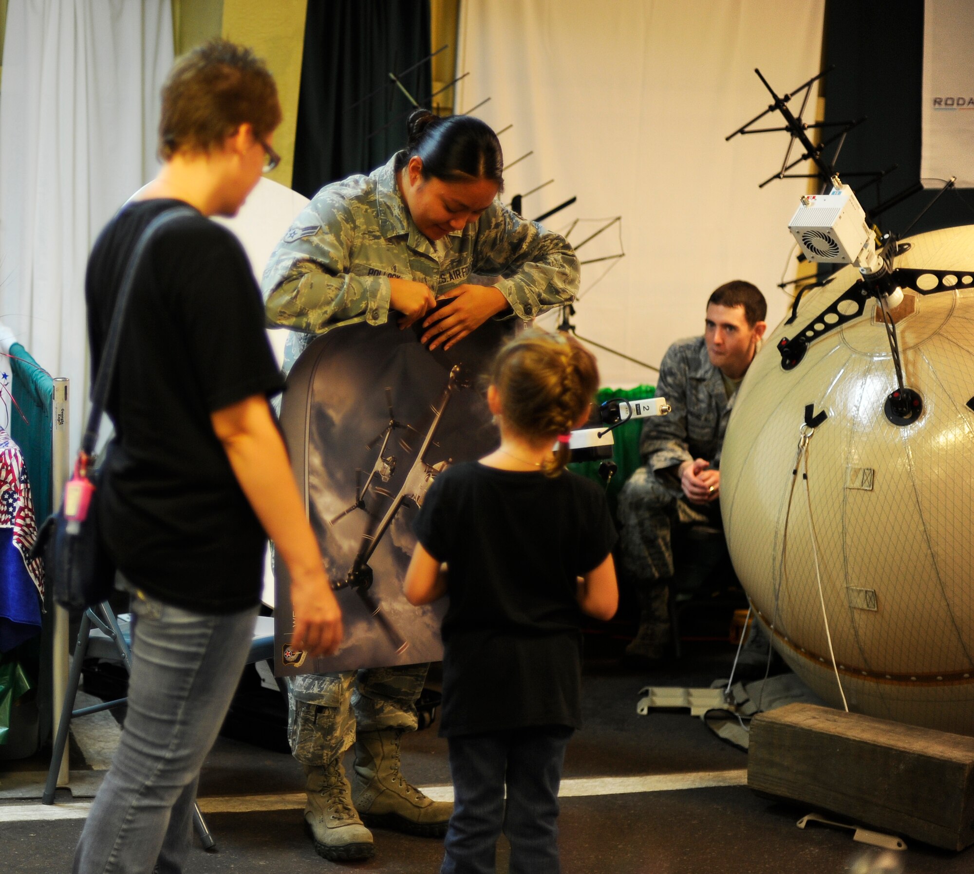 Airman 1st Class Theresa Pollock, 1st Special Operations Communications Squadron cyber systems operator, rolls up a poster of CV-22 Ospreys for a little girl during the 2014 Northwest Florida Tri-County Fair at the Fort Walton Beach Fairgrounds in Fort Walton Beach, Fla., Oct. 2, 2014. The 1st SOCS displayed an array of tactical antennas that can deploy and pull mission services anywhere around the world. (U.S. Air Force photo/Staff Sgt. Sarah Hanson)