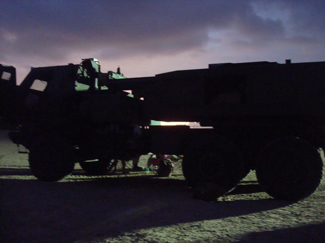 A M142 HIMARS launcher from Battery R is silhouetted against a sunset  at Kailua Pier as it awaits embarkation aboard the USS Peleliu (LHA-5).
