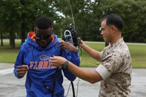 Staff Sgt. Samuel Beltram, the training chief with Explosive Ordnance Disposal Company, 8th Engineer Support Battalion, 2nd Marine Logistics Group, and a native of Fort Worth, Texas,  helps a student of Lejeune High School put on the gear to operate one of the robots on display, Oct. 3, 2014.  Approximately 60 students, ranging from freshmen to seniors, packed the classroom to hear how the Marines use robotics on the battlefield and how engineering can better people’s lives. The school requested the Marines give the demonstration because the students are beginning their robotics curriculum of the Bio-Tech Department course of study. (U.S. Marine Corps photo by Cpl. Michael Dye / Released)