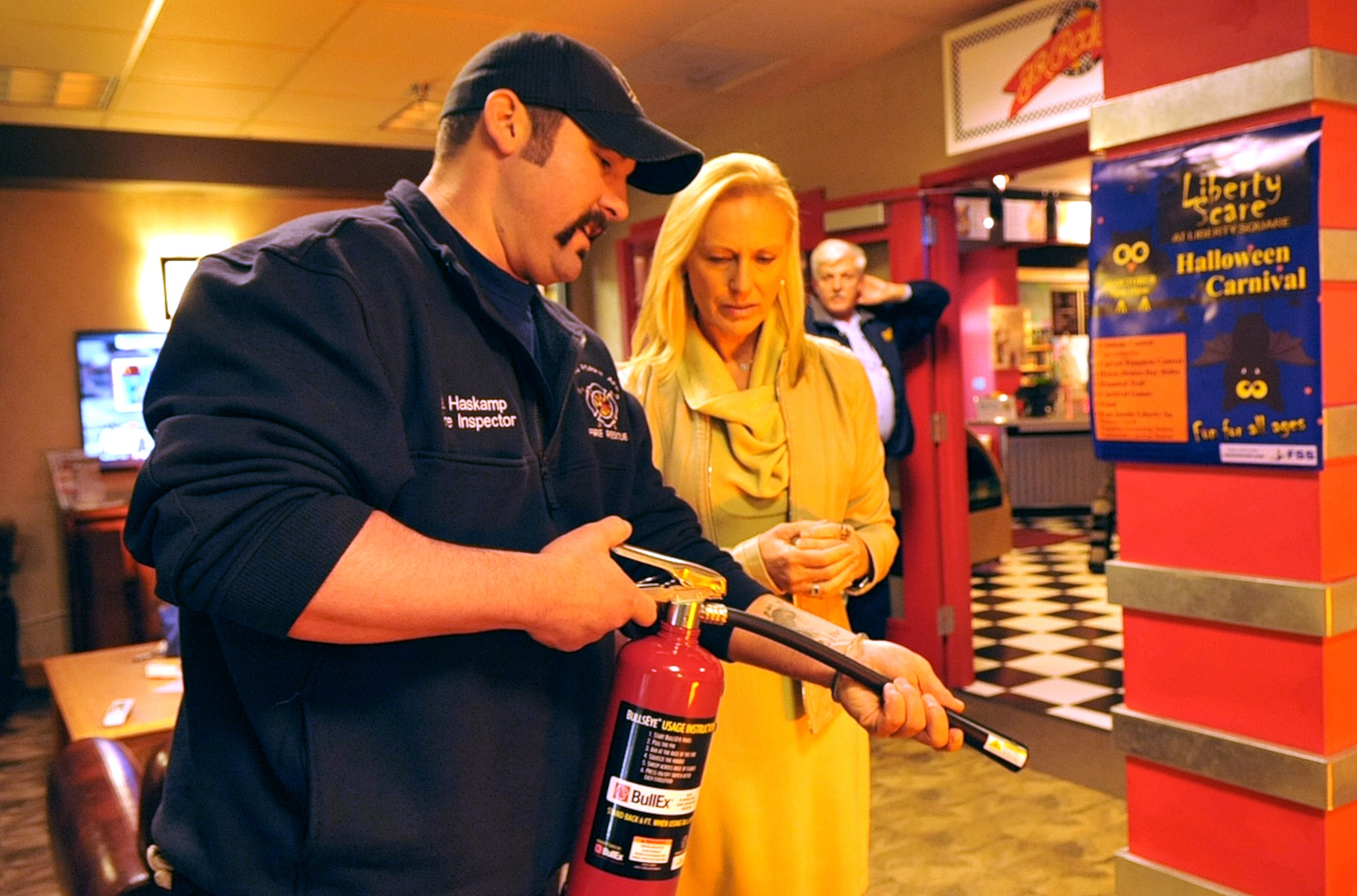 Justin Haskamp (left), Grand Forks Air Force Base Fire Department fire inspector, teaches Julie McWalter, 319th Force Support Squadron marketing director, the proper way to use a basic, portable fire extinguisher Oct. 8, 2014, at the Northern Lights Club at Grand Forks AFB, N.D. The Grand Forks AFB Fire Department kicked off Fire Prevention week October 3, which runs October 11. (U.S. Air Force photo/Airman 1st Class Bonnie Grantham)