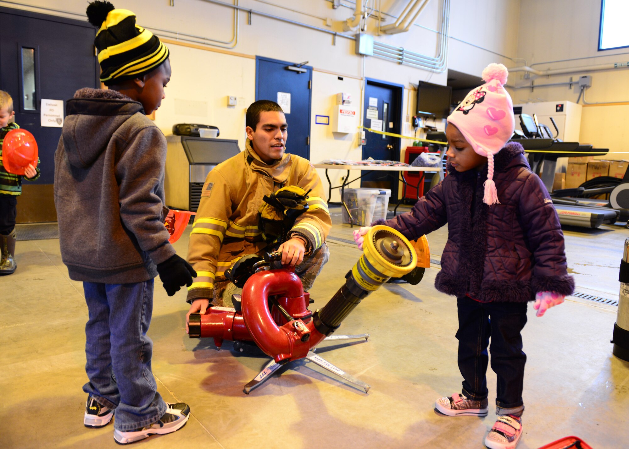 Camden and Aevyn Wyke investigate a fire hose with Airman 1st Class Israel Hernandez, 354th Civil Engineer Squadron firefighter, during the Eielson Fire Department open house Oct. 5, 2014, Eielson Air Force Base, Alaska. The open house kicked off Fire Prevention Week which has been observed nation-wide since 1922 to commemorate the Great Chicago Fire of 1871. (U.S. Air Force photo by Senior Airman Ashley Nicole Taylor/Released)