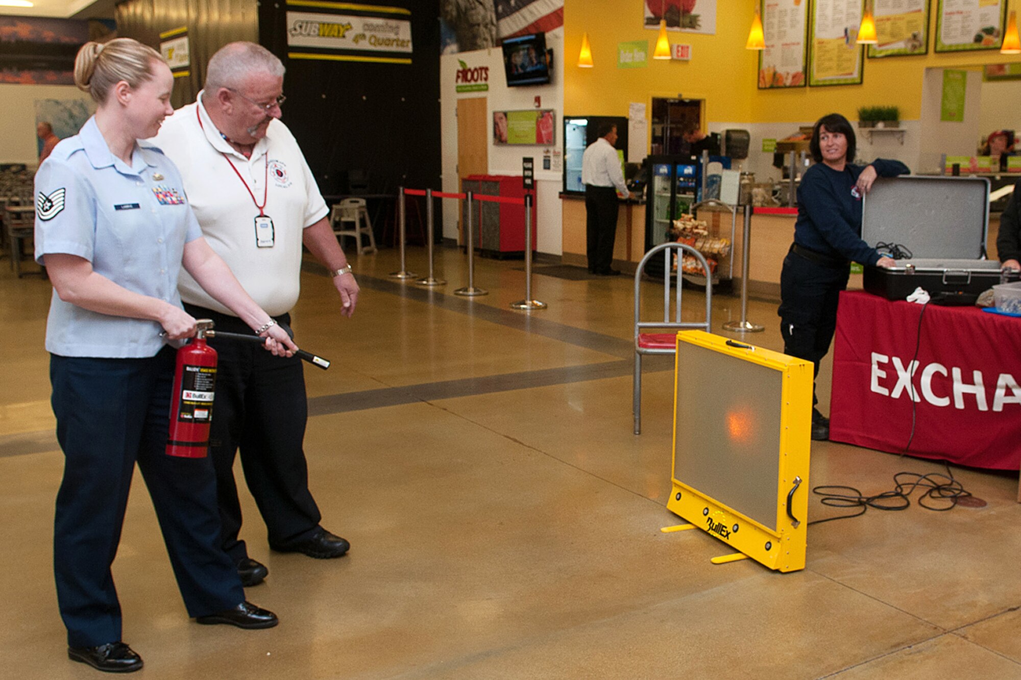 Robert Kenyon, Hanscom Fire Prevention captain, instructs Tech. Sgt. Jessica Labrie, Battle Management Directorate Operations Management NCO in charge, on the proper use of a fire extinguisher during a Fire Prevention Week activity at the Base Exchange Oct. 7. Throughout the week, the Hanscom Fire Department recognized the annual fire prevention week Oct. 5 through 11 by reminding employees and residents to tests their fire alarm monthly. (U.S. Air Force photo by Linda LaBonte Britt)
