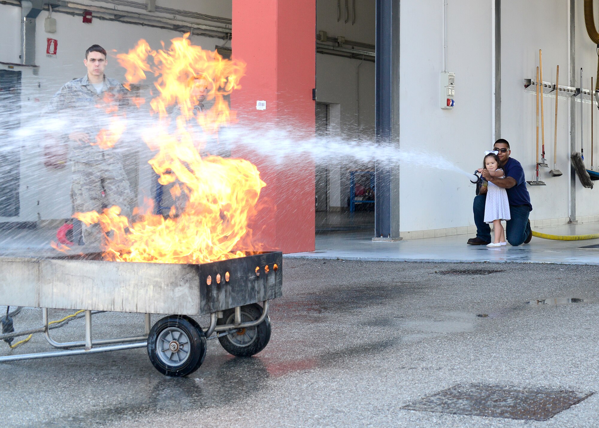 Senior Airman Manuel Rodriguez, 31st Civil Engineer Squadron firefighter, shows a child how to put out a fire during a fire department open house, Oct. 5, 2014, at Aviano Air Base, Italy. National Fire prevention Week was established to commemorate the Great Chicago Fire of 1871, which killed 300 people, left 100,000 homeless, destroyed 17,400 structures and burned 2,000 acres. (U.S. Air Force photo/Senior Airman Michael Battles)